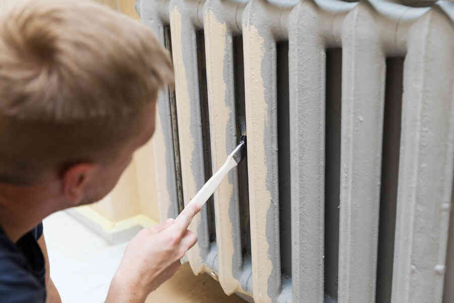 A radiator being painted the same colour as the surrounding wall.